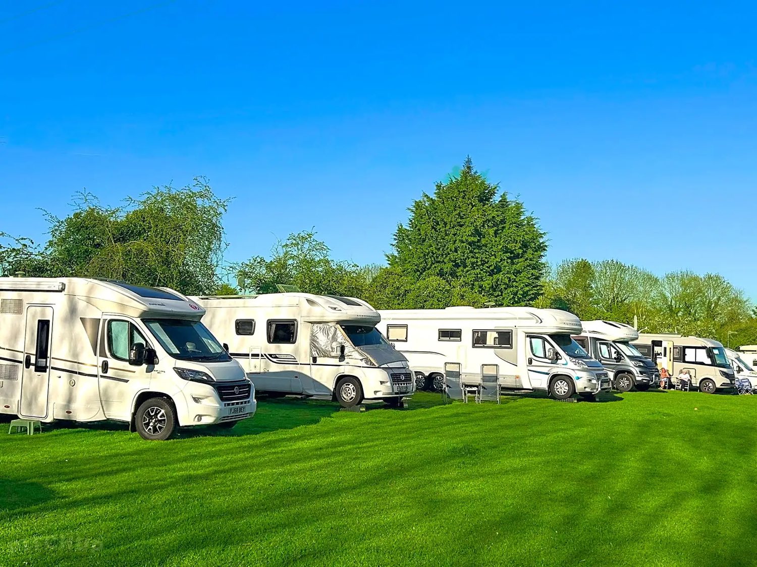 Motorhomes and campervans pitched on the grass at The Cottage of Content campsite under a clear sky.