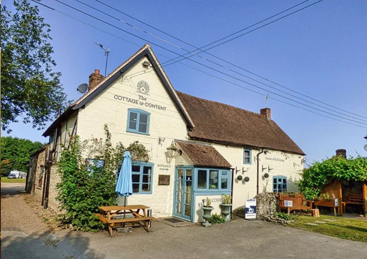 The Cottage of Content - a whitewashed country pub with duck-egg blue windows and picnic benches out front.